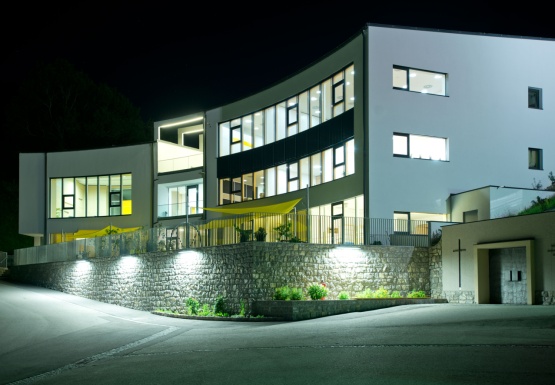 Ein halbrundes Gebäude bei Nacht. Die Fenster leuchten hell.