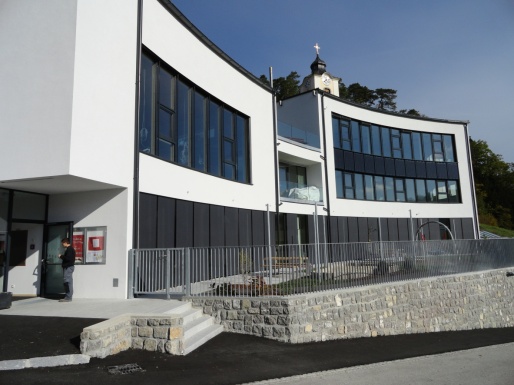 Seitliche Außenaufnahme eines weißen Kindergartengebäudes mit vielen Fenstern.